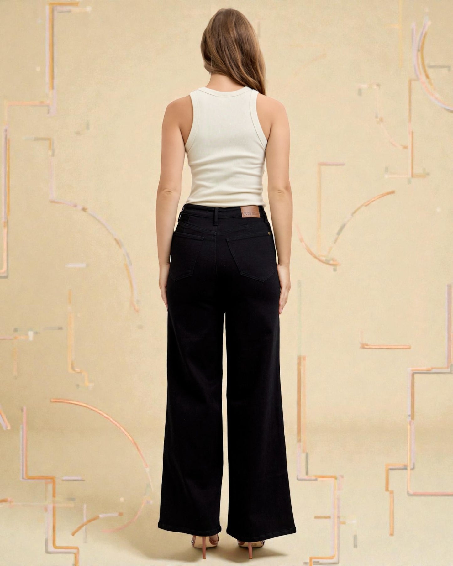 Woman wearing a white sleeveless top and black wide-leg pants against a beige background