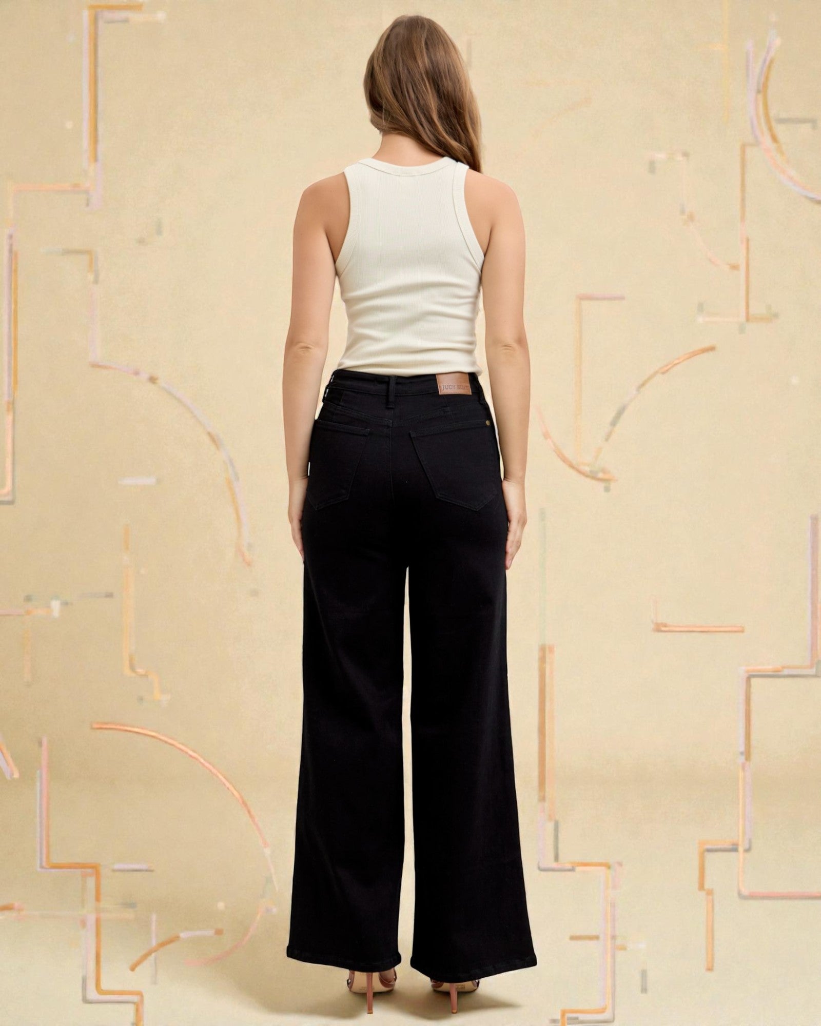 Woman wearing a white sleeveless top and black wide-leg pants against a beige background