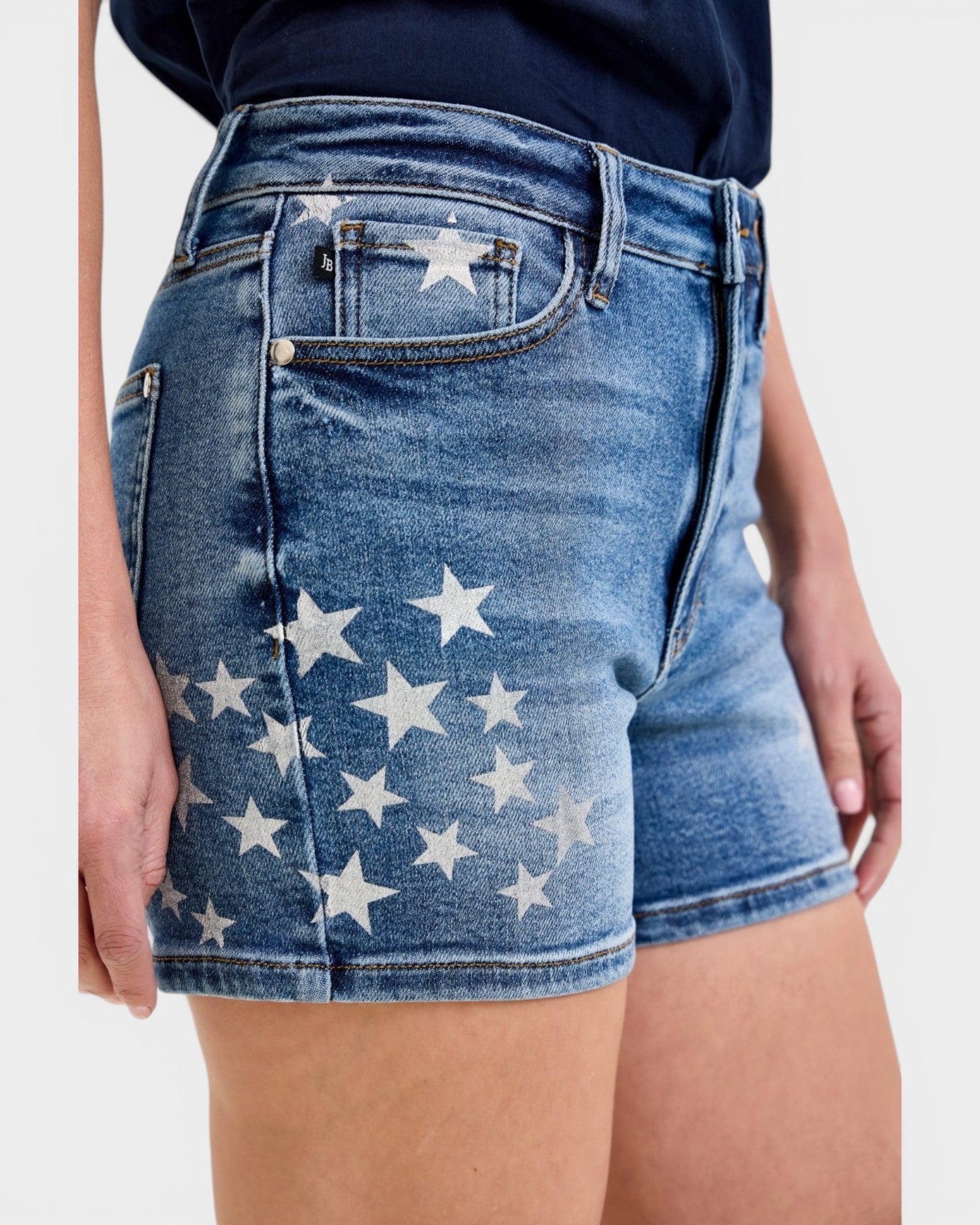 Blue denim shorts with white star pattern worn by a person on a plain background