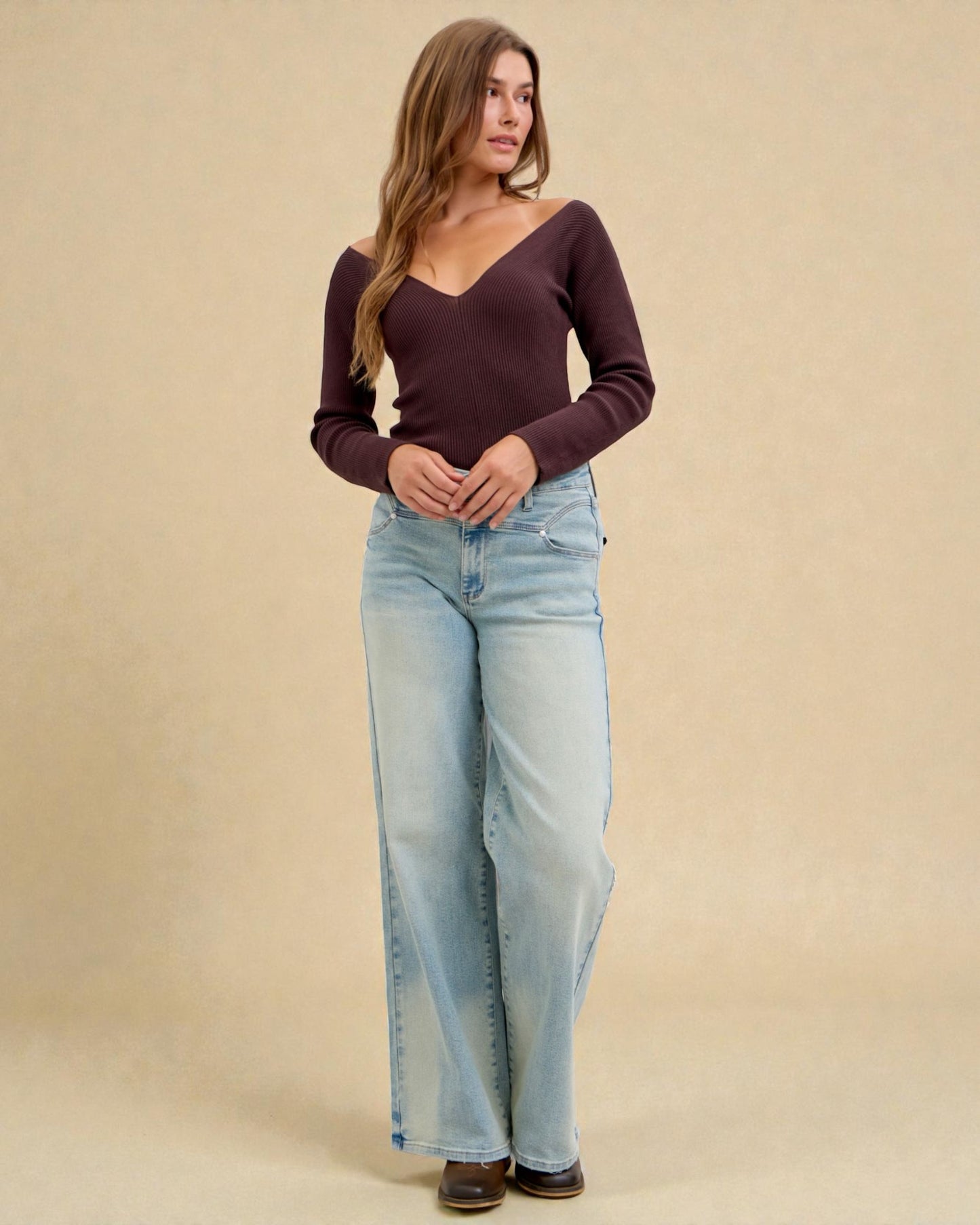 Woman wearing a dark purple long-sleeve top and light blue jeans against a beige background