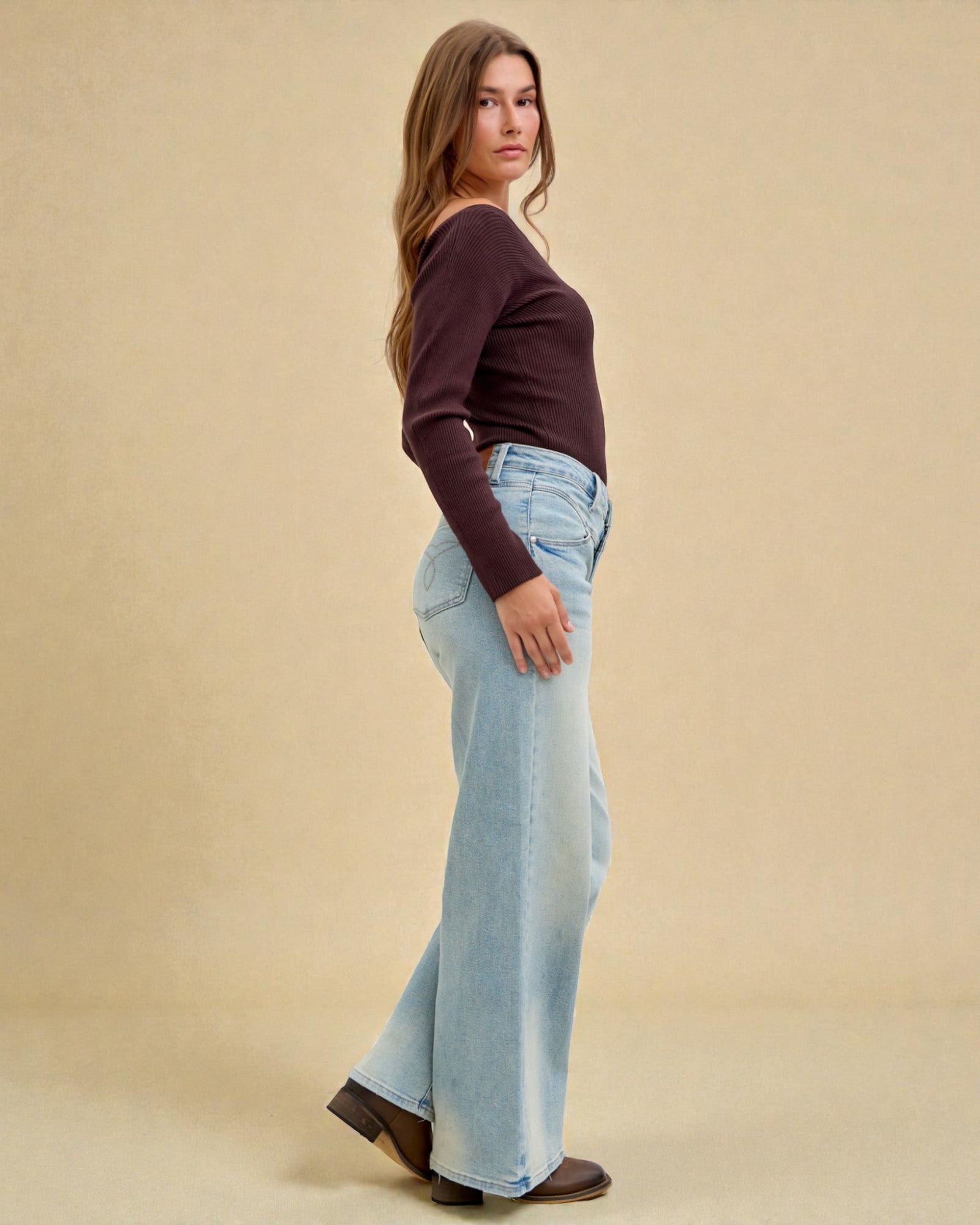 Woman wearing a brown top and light blue jeans against a beige background