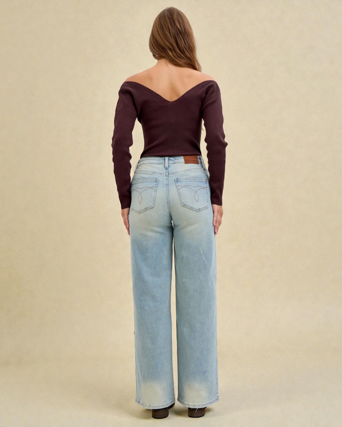 Woman wearing a burgundy off-shoulder top and light blue jeans on a beige background