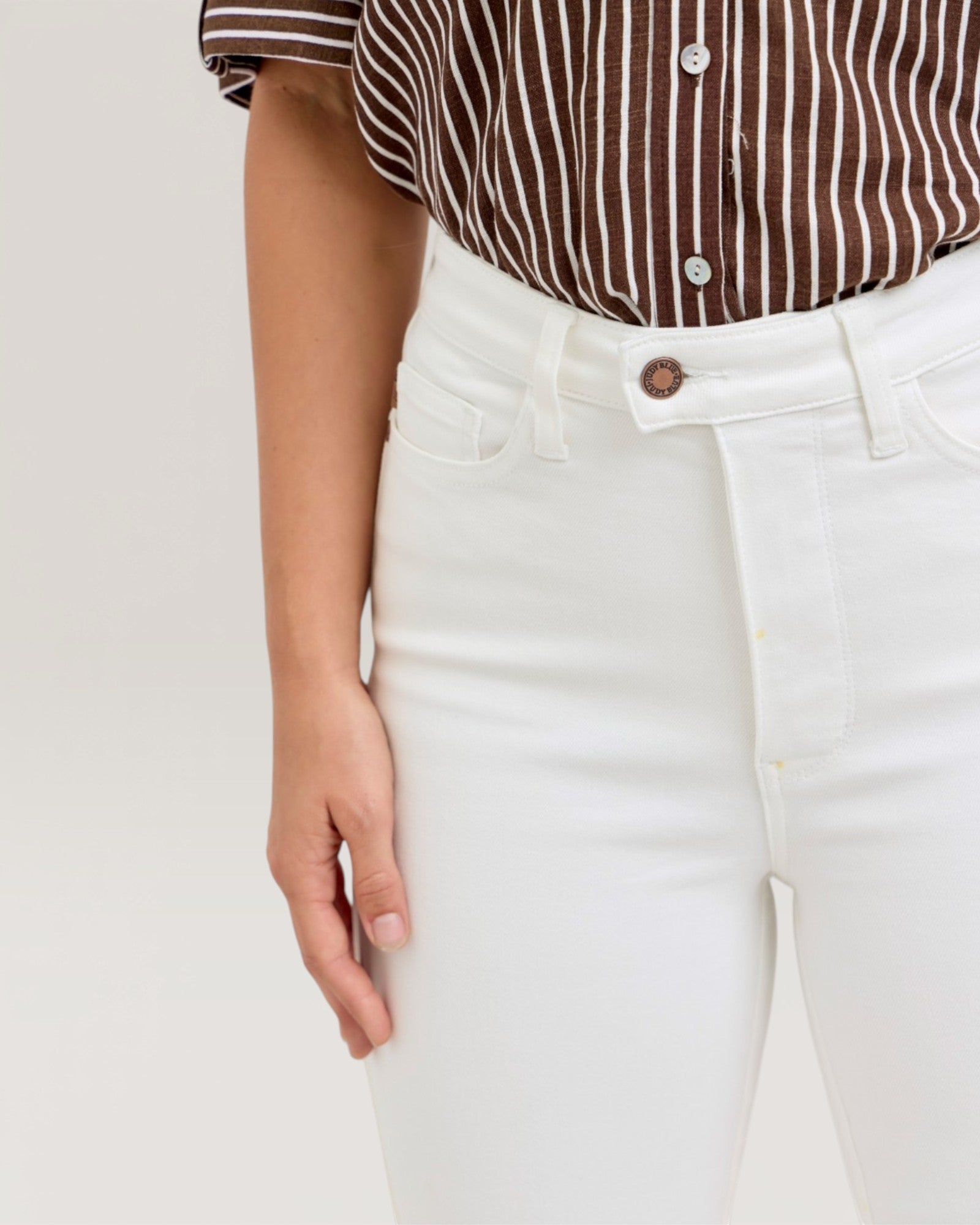 Person wearing a brown and white striped shirt and white pants on a light beige background