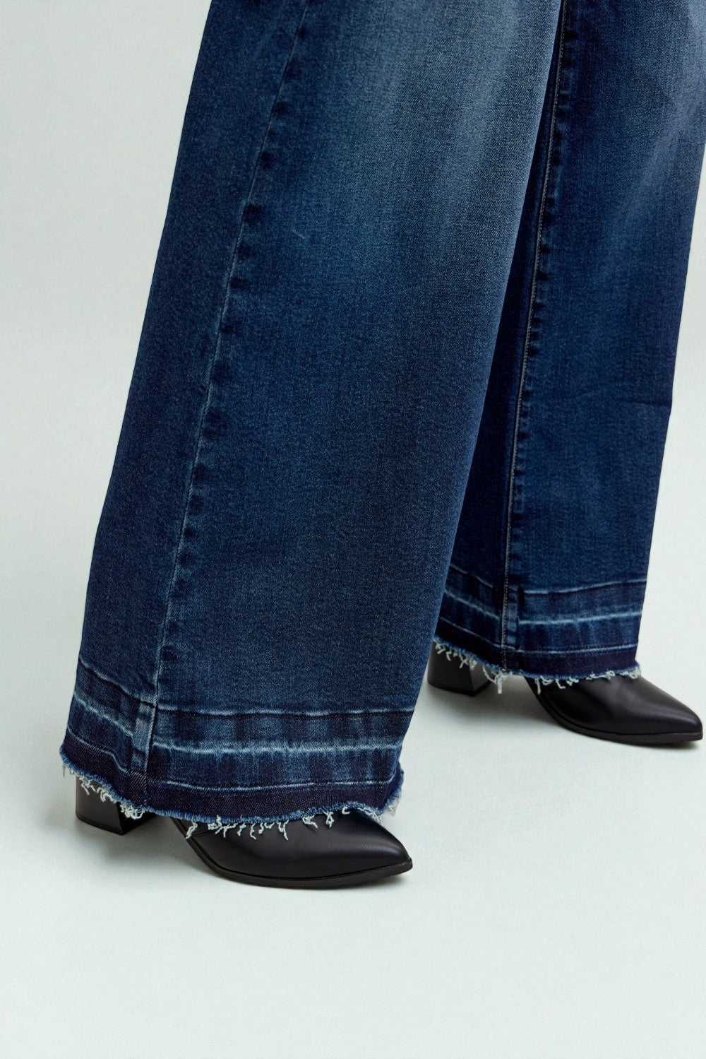Close-up of blue jeans with frayed hem and black shoes on a light gray background