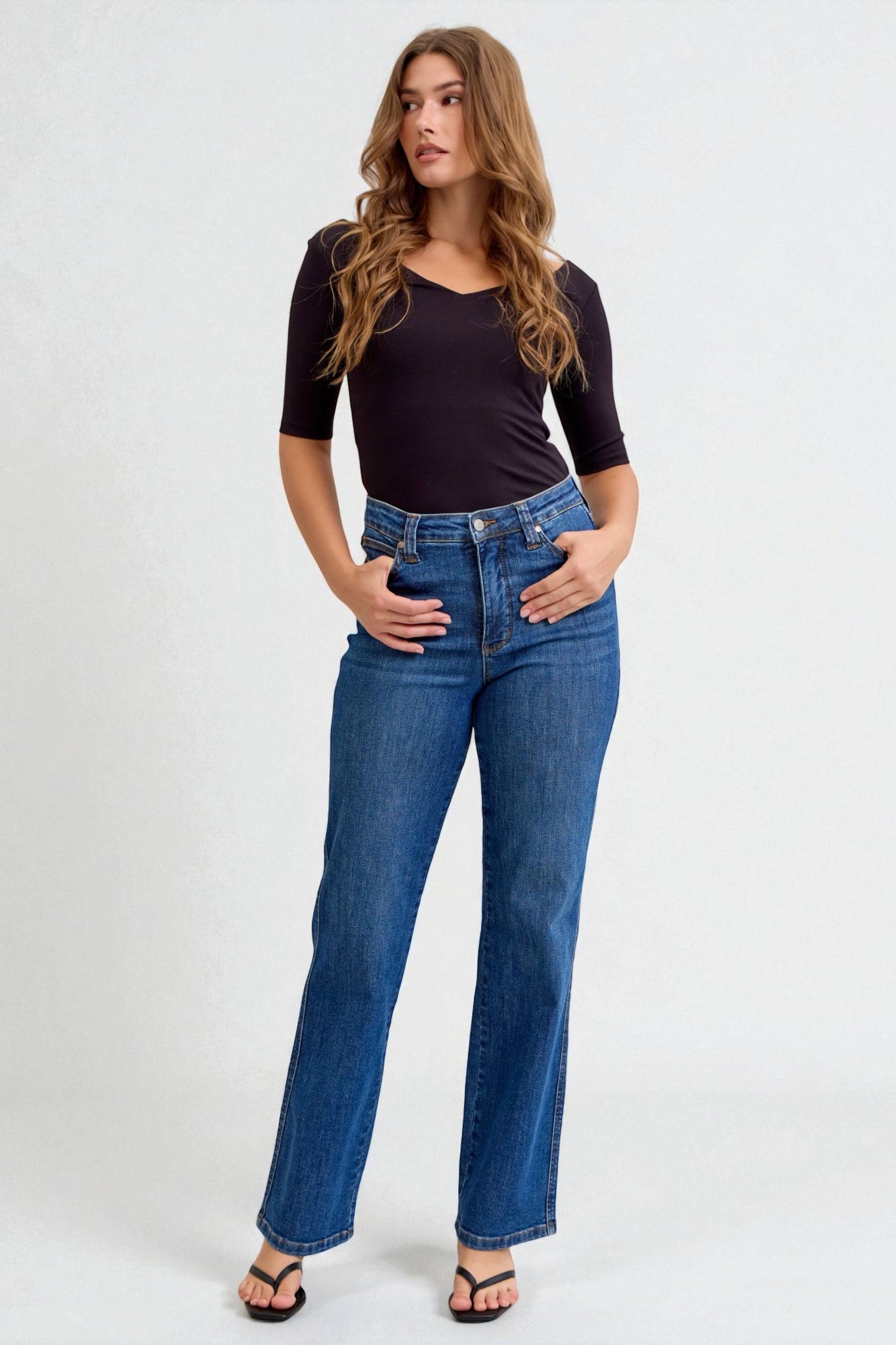 Woman wearing a black top and blue jeans on a white background