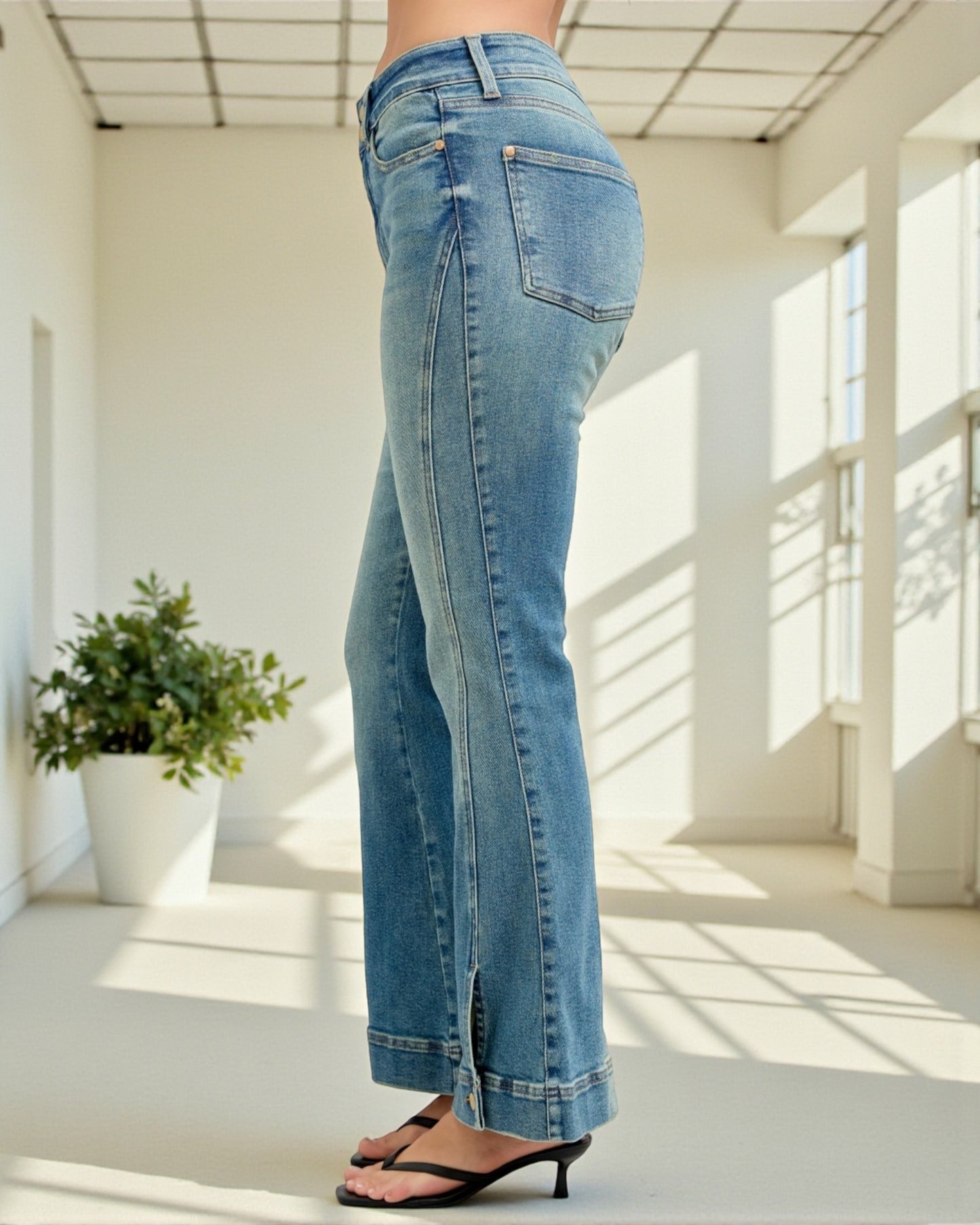 Person wearing blue jeans standing in a bright room with large windows.