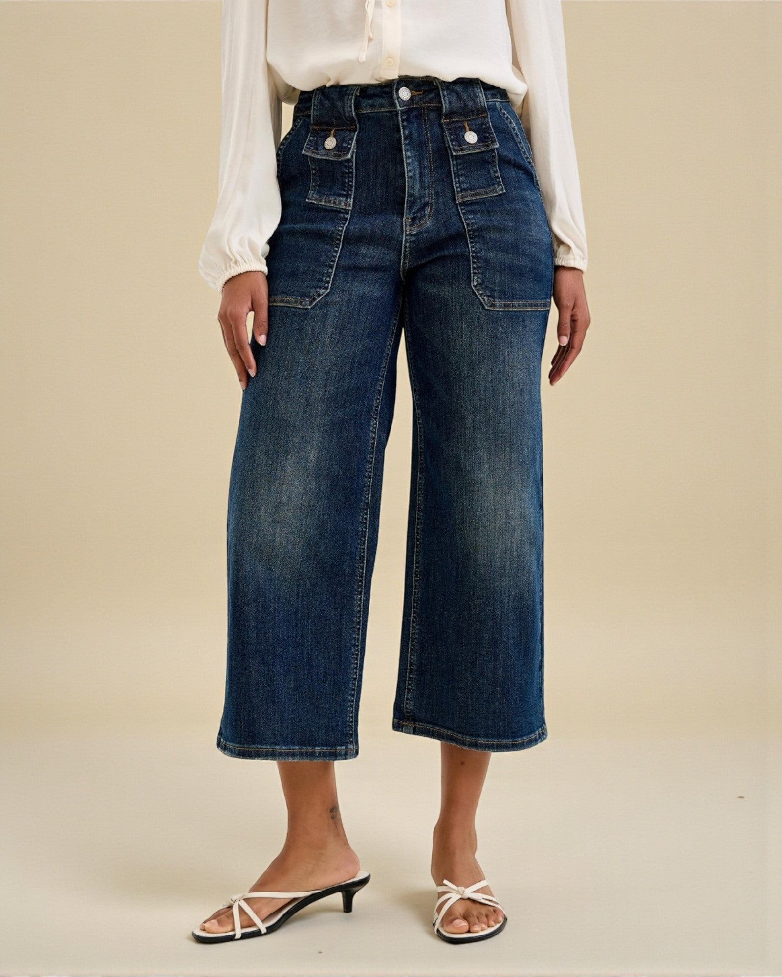 Person wearing blue wide-leg jeans and a white shirt on a beige background