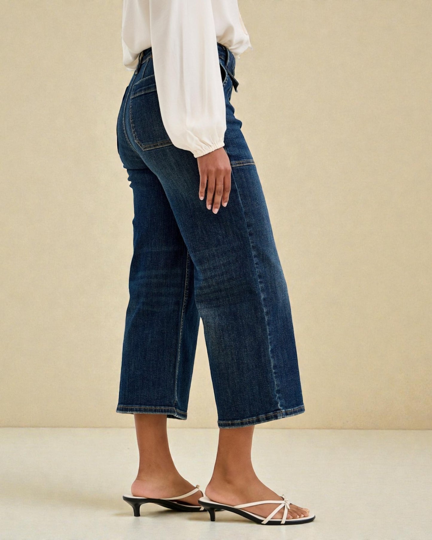 Person wearing blue jeans and a white blouse on a beige background
