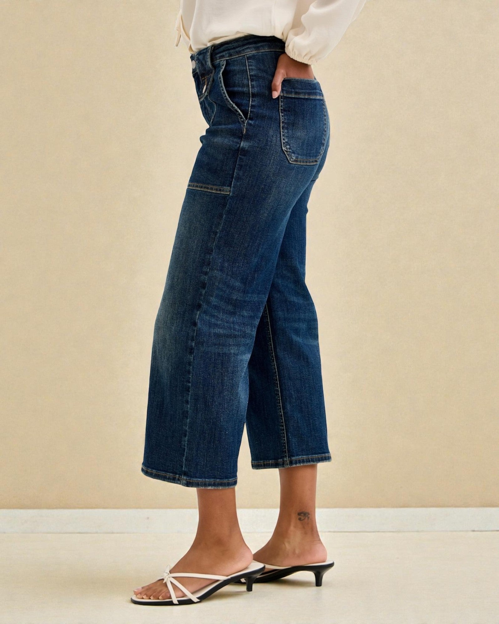 Person wearing blue jeans and a white blouse against a beige background