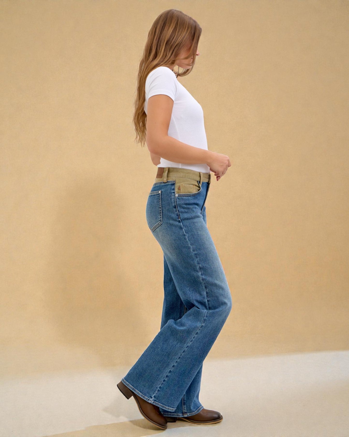 Woman wearing blue flared jeans and a white shirt on a beige background