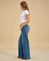 Woman wearing blue jeans and a white t-shirt against a beige background