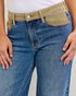Close-up of blue jeans with a beige belt and pocket on a light gray background