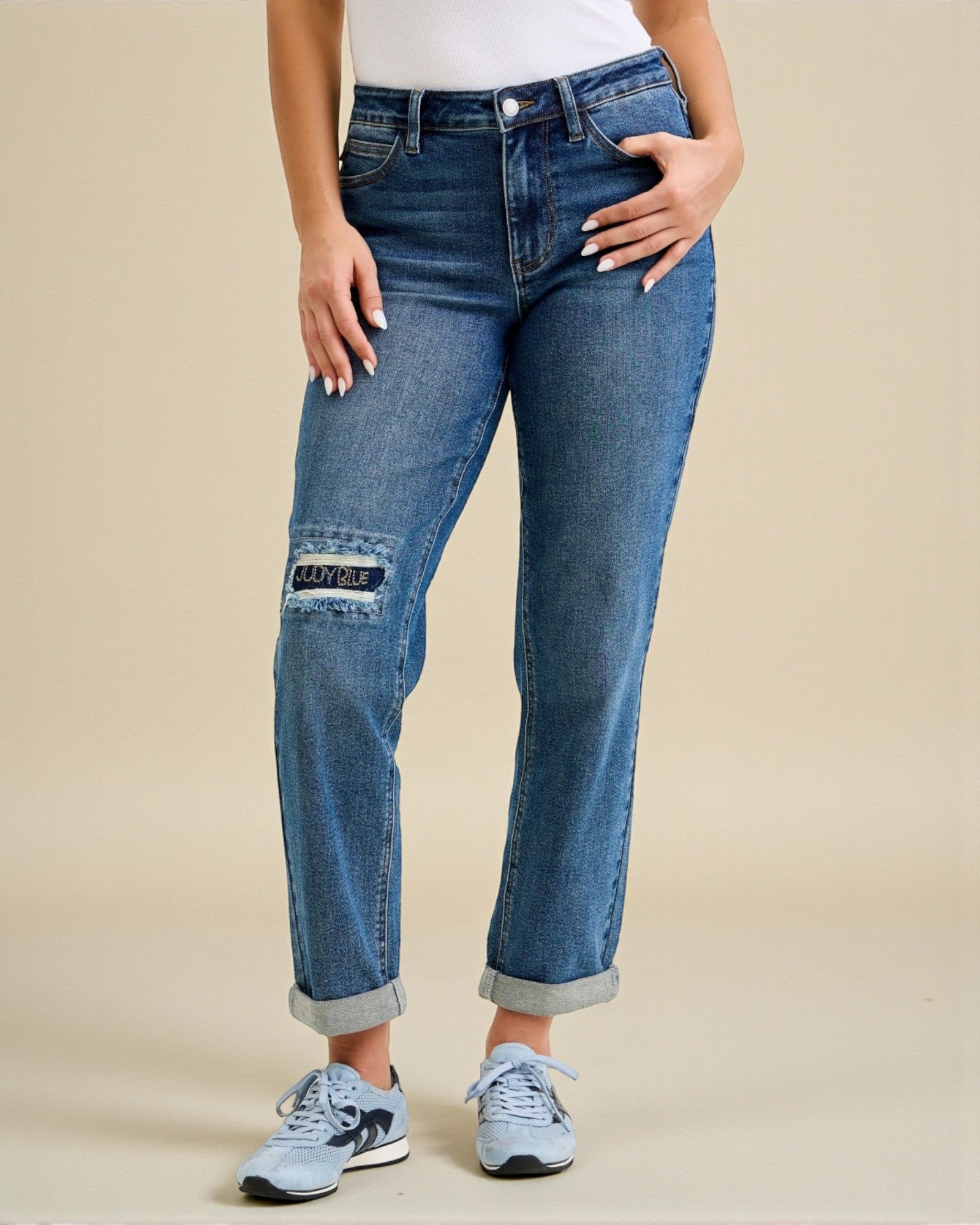 Person wearing blue jeans with patch details on a beige background