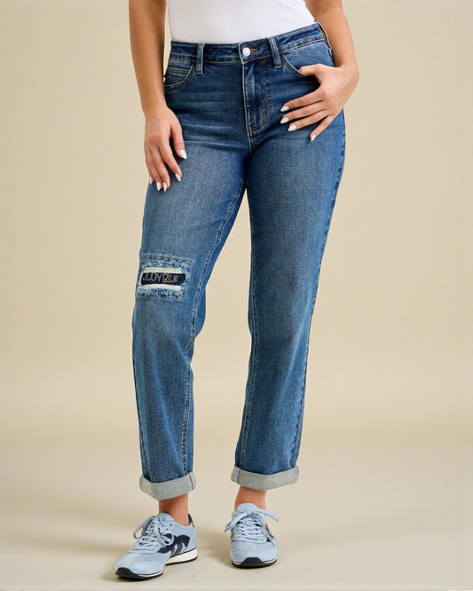 Person wearing blue jeans with patch details on a beige background