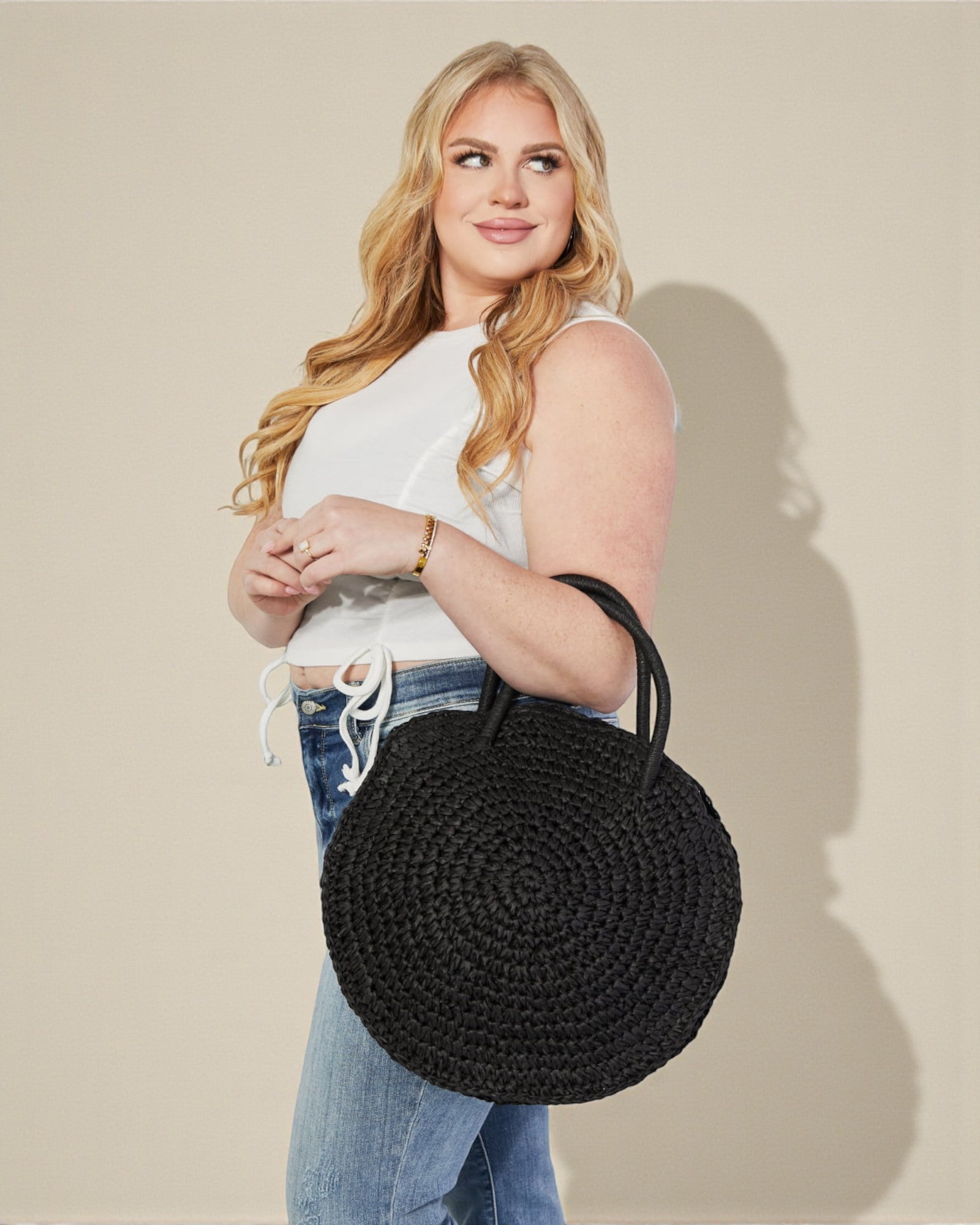 Woman holding a black woven handbag against a beige background