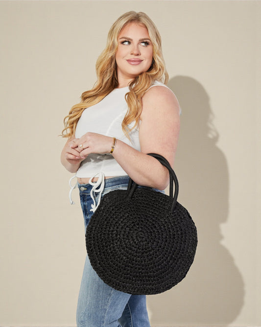 Woman holding a black woven handbag against a beige background
