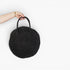 A hand holding a round black woven straw bag with two top handles against a plain white background.