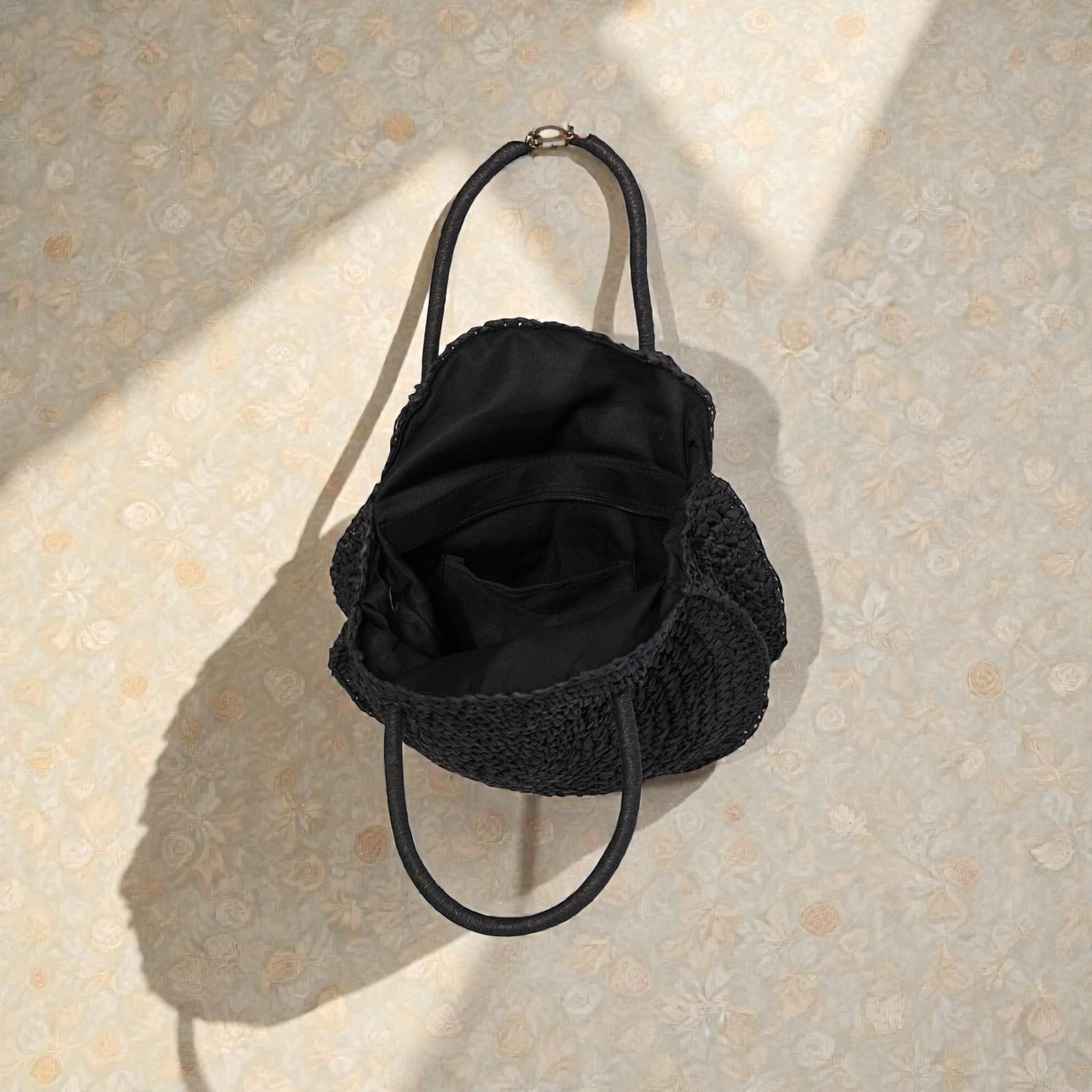 Black handbag with textured handle on a beige textured surface