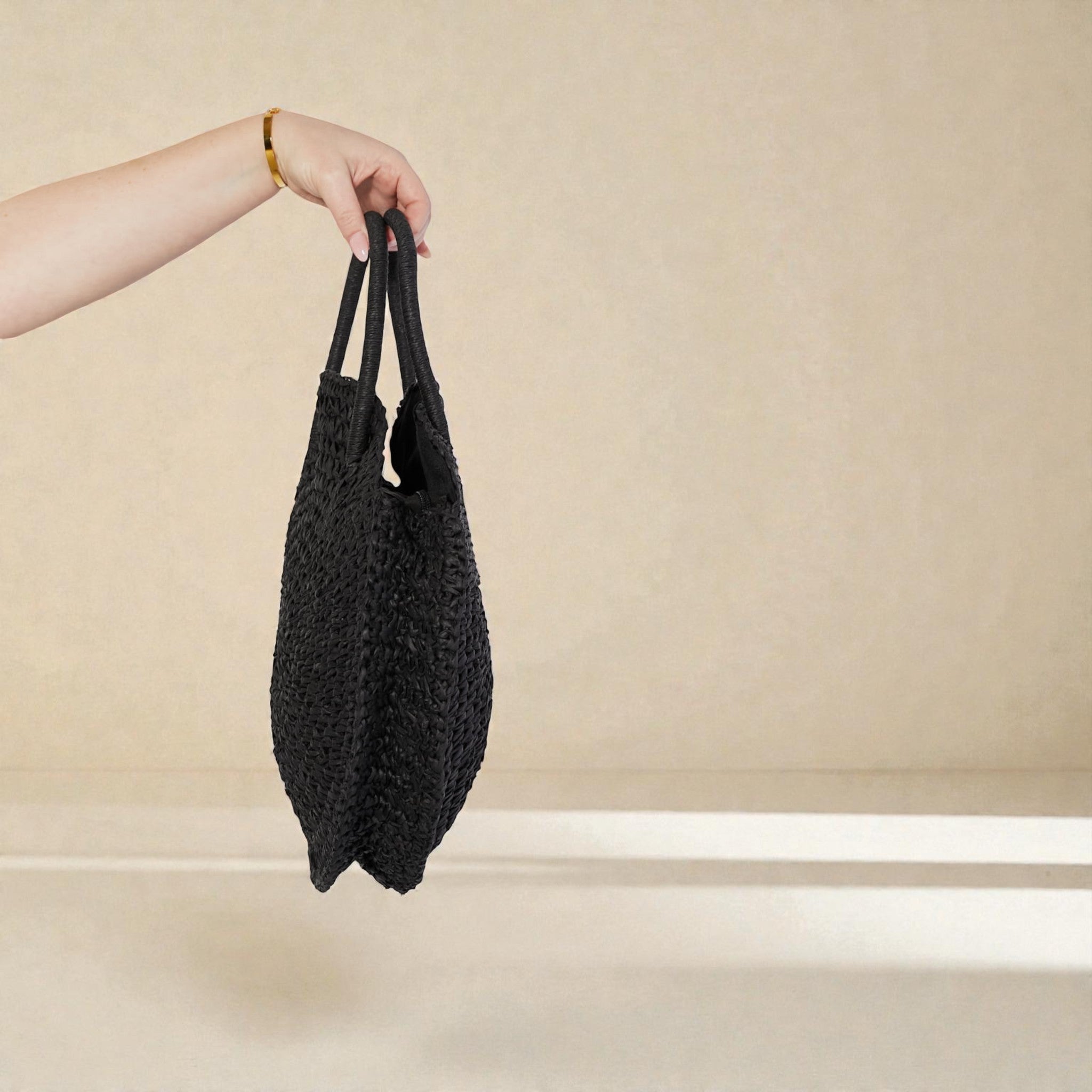 Black textured tote bag held by a hand against a beige background