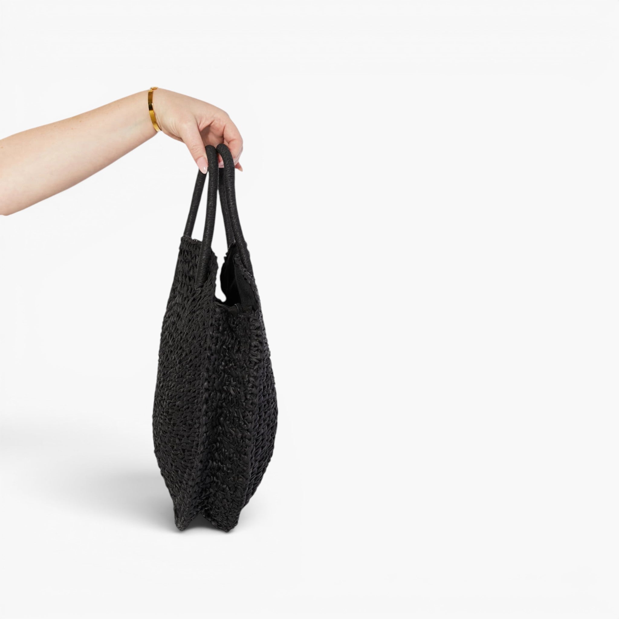 A black textured woven tote bag held by a person's hand against a clean white background.