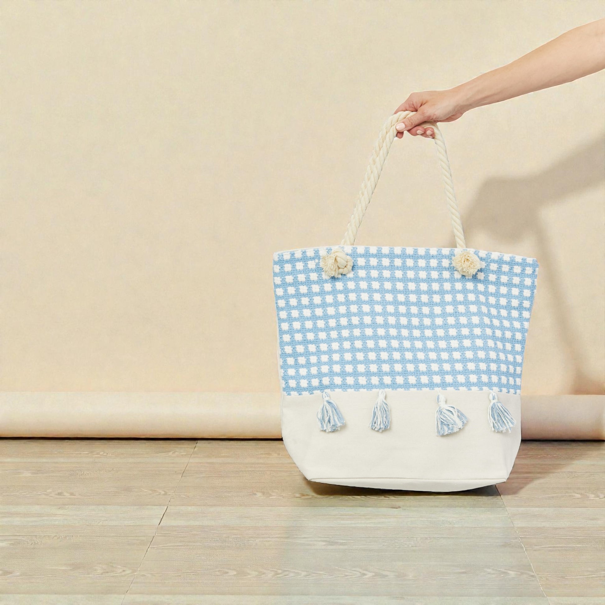 Blue and white checkered bag with tassels held by a hand on a beige background