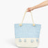 A light blue and white gingham tote bag with cream rope handles and tassels, held by a person's hand against a plain white background.