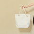 White tote bag with rope handles held by a person against a beige background