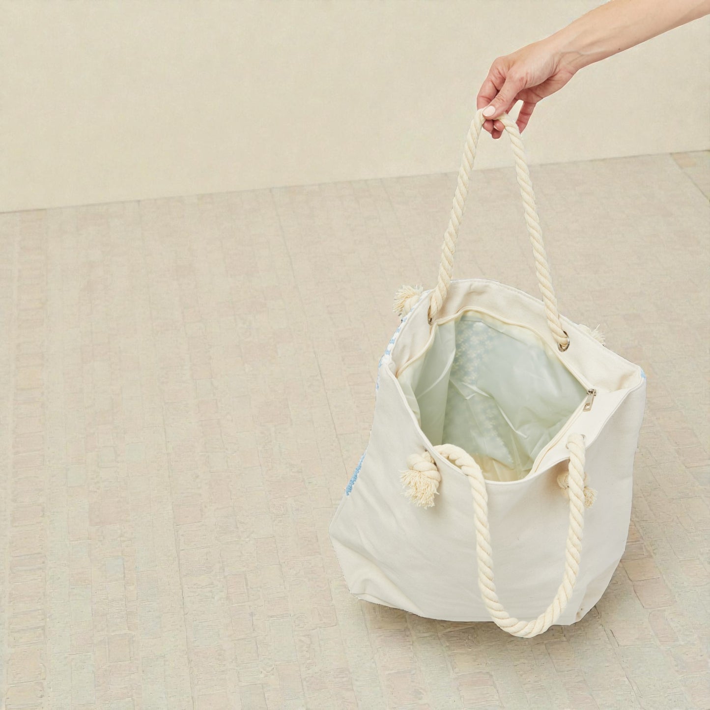 White drawstring bag with rope handles held by a hand on a beige background