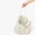 An off-white canvas tote bag with thick cream rope handles, held by a hand against a plain white background.