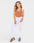 Woman wearing a brown tank top and white jeans on a plain background