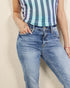 Person wearing a striped tank top and blue jeans against a beige background