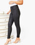 A model wearing black high-waisted skinny jeans with a button-fly front, paired with a white top and beige high-heeled sandals, standing next to a white wooden dresser.