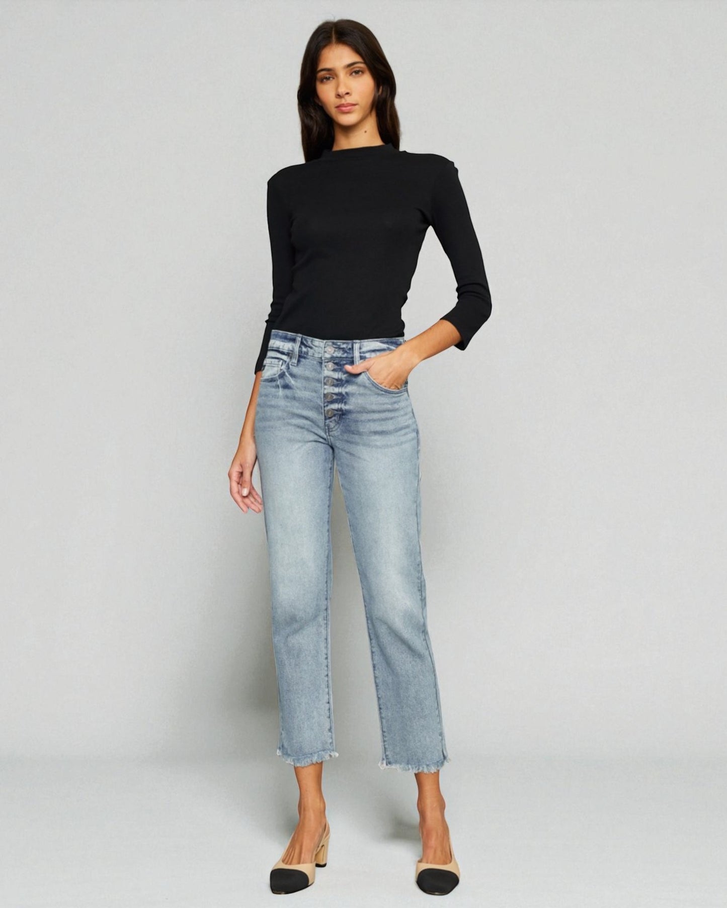 Woman wearing a black top and light blue jeans on a gray background