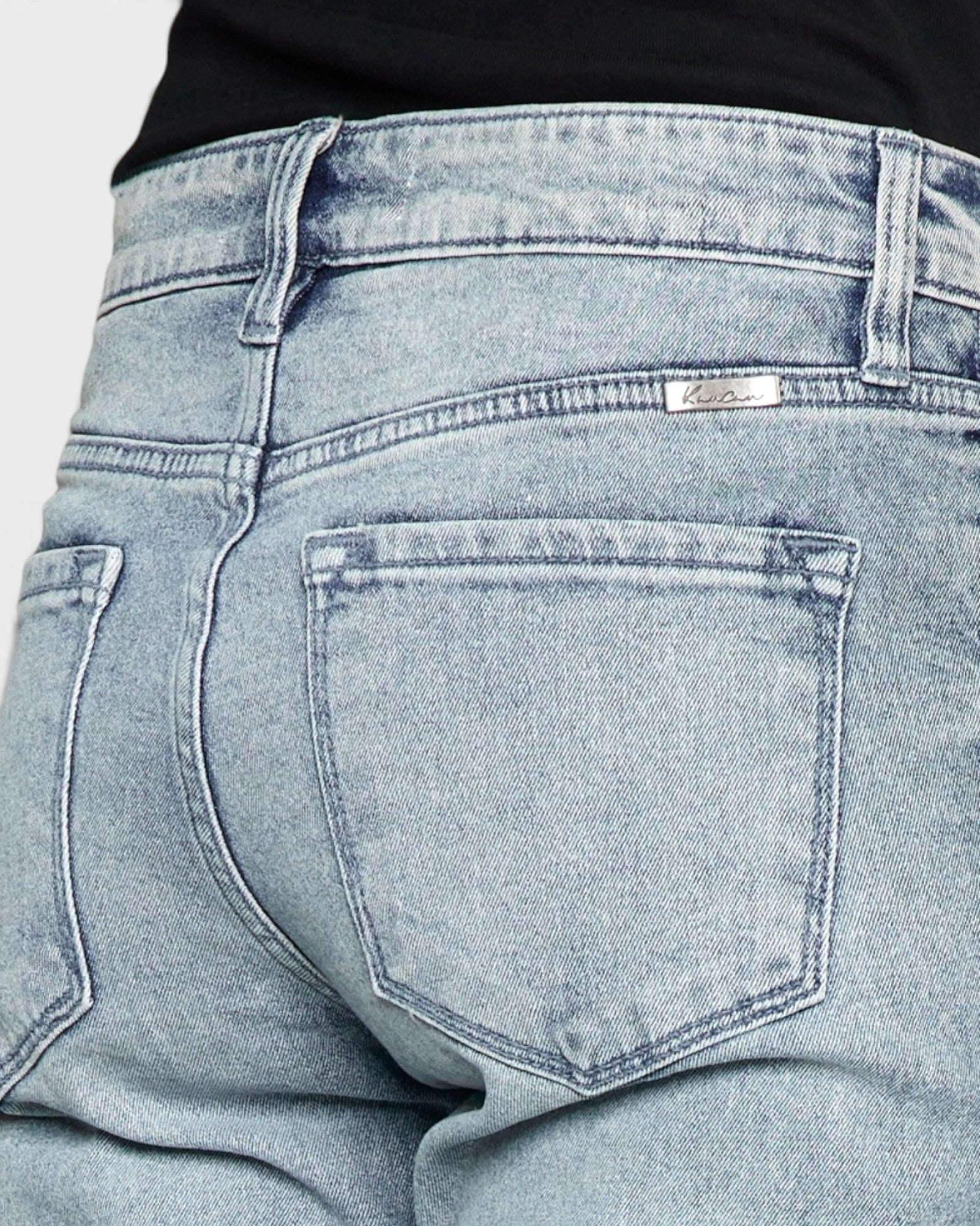 Close-up of light blue denim jeans with a brand label on a plain background