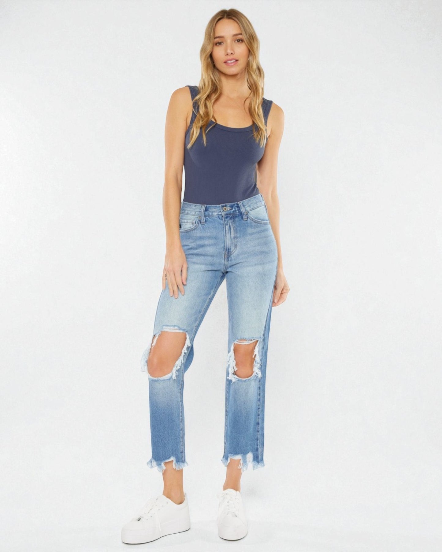 Woman wearing a navy tank top and distressed blue jeans on a white background
