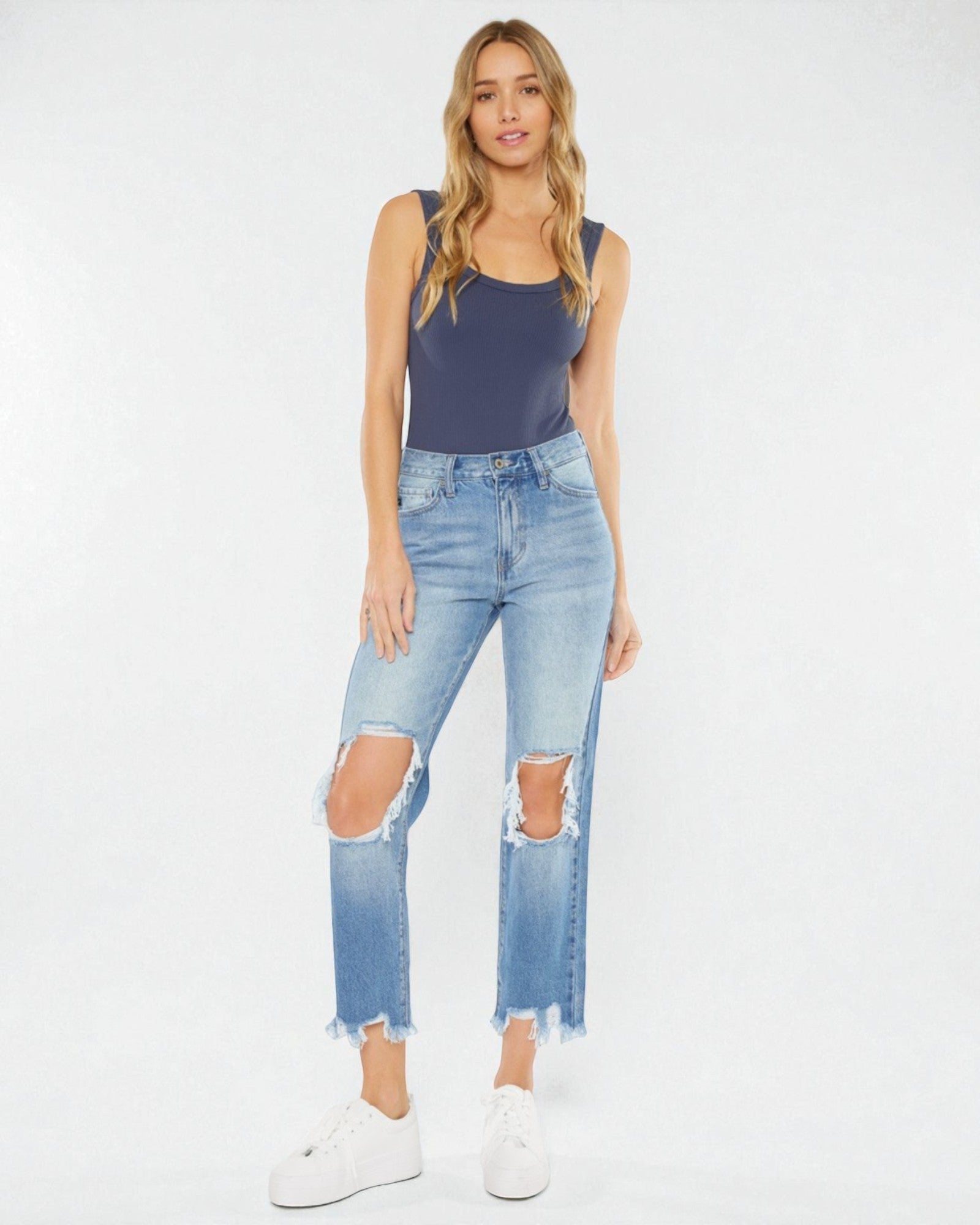 Woman wearing a navy tank top and distressed blue jeans on a white background