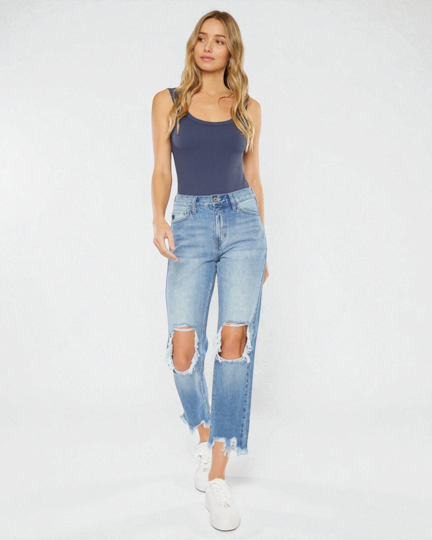 Woman wearing a navy tank top and light blue ripped jeans on a white background