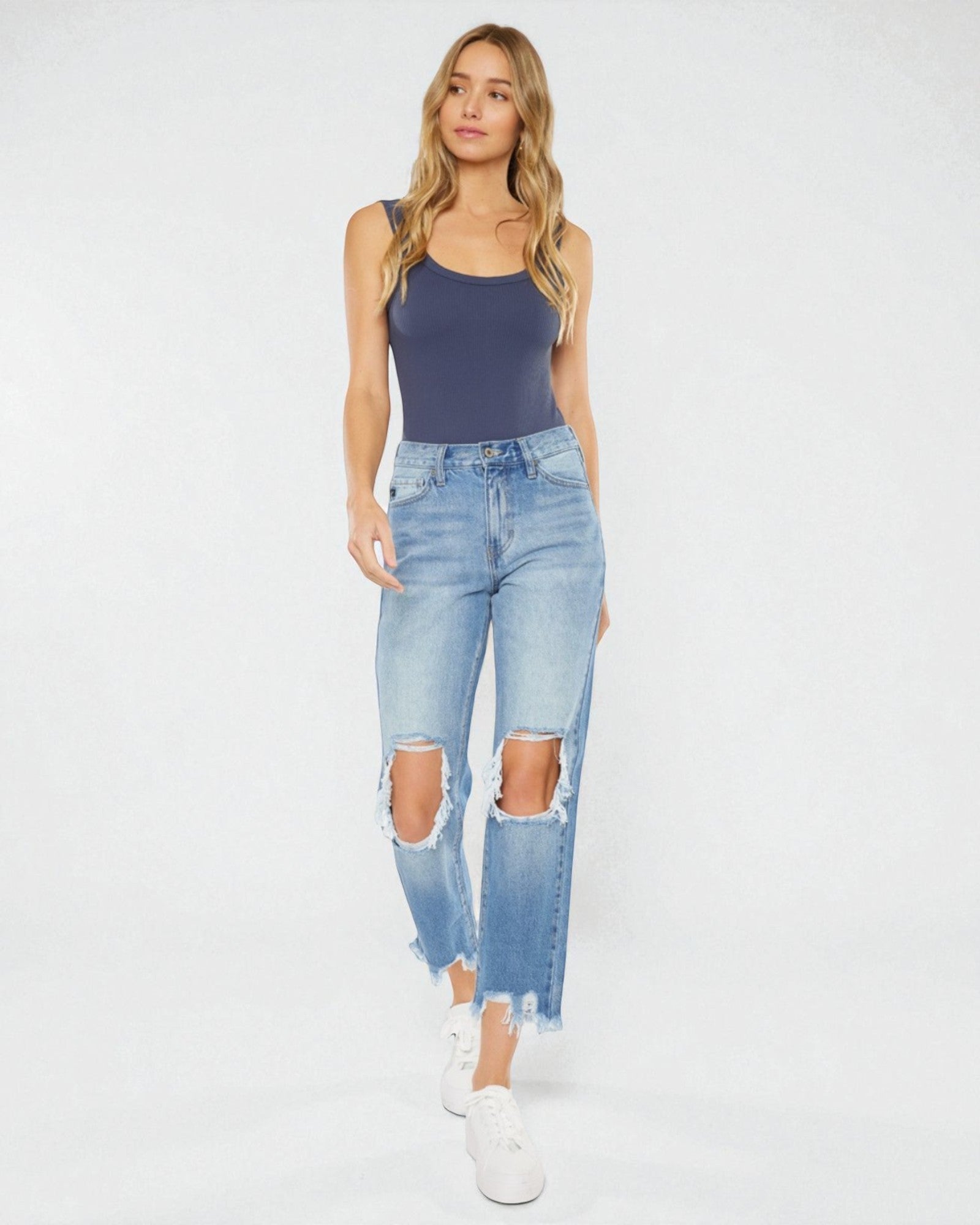 Woman wearing a navy tank top and light blue ripped jeans on a white background