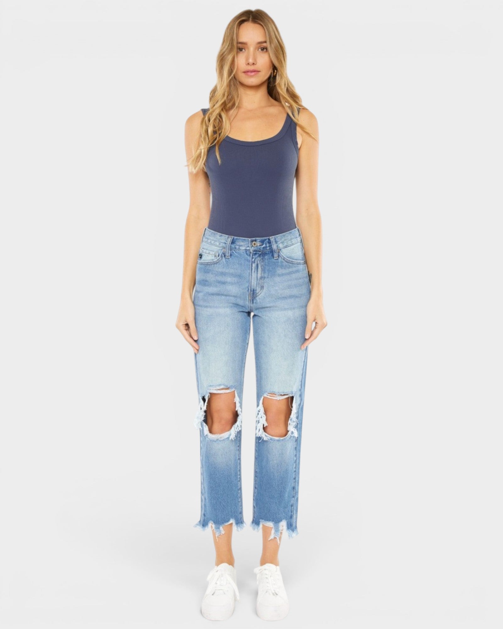 Woman wearing a dark blue tank top and light blue ripped jeans on a white background