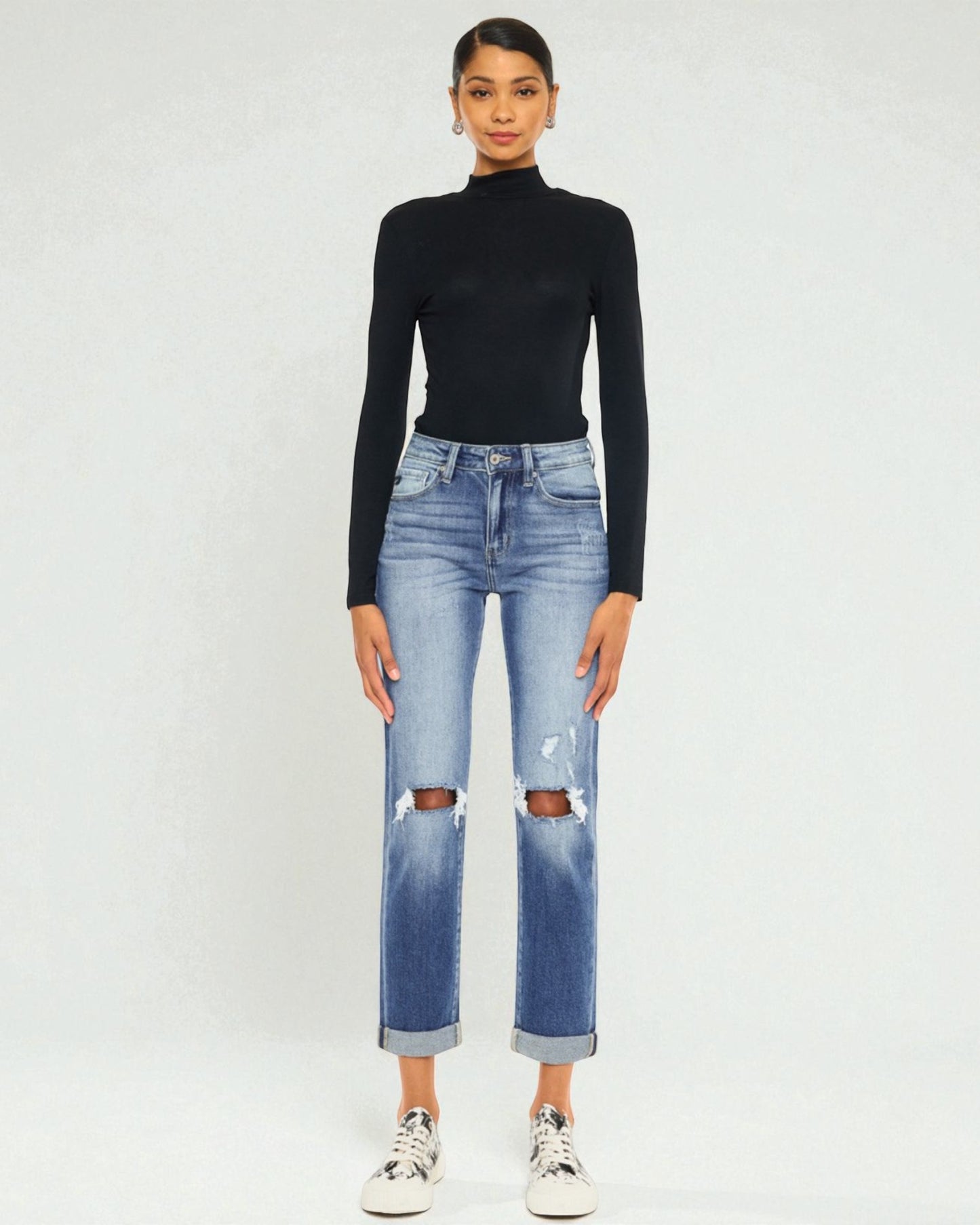 Person wearing a black turtleneck and blue ripped jeans on a white background