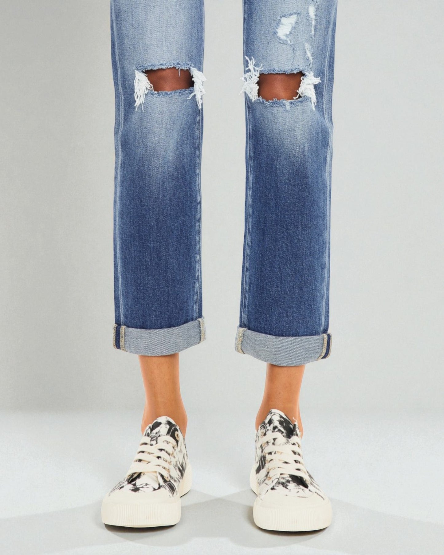 Ripped blue jeans worn with white sneakers on a plain background