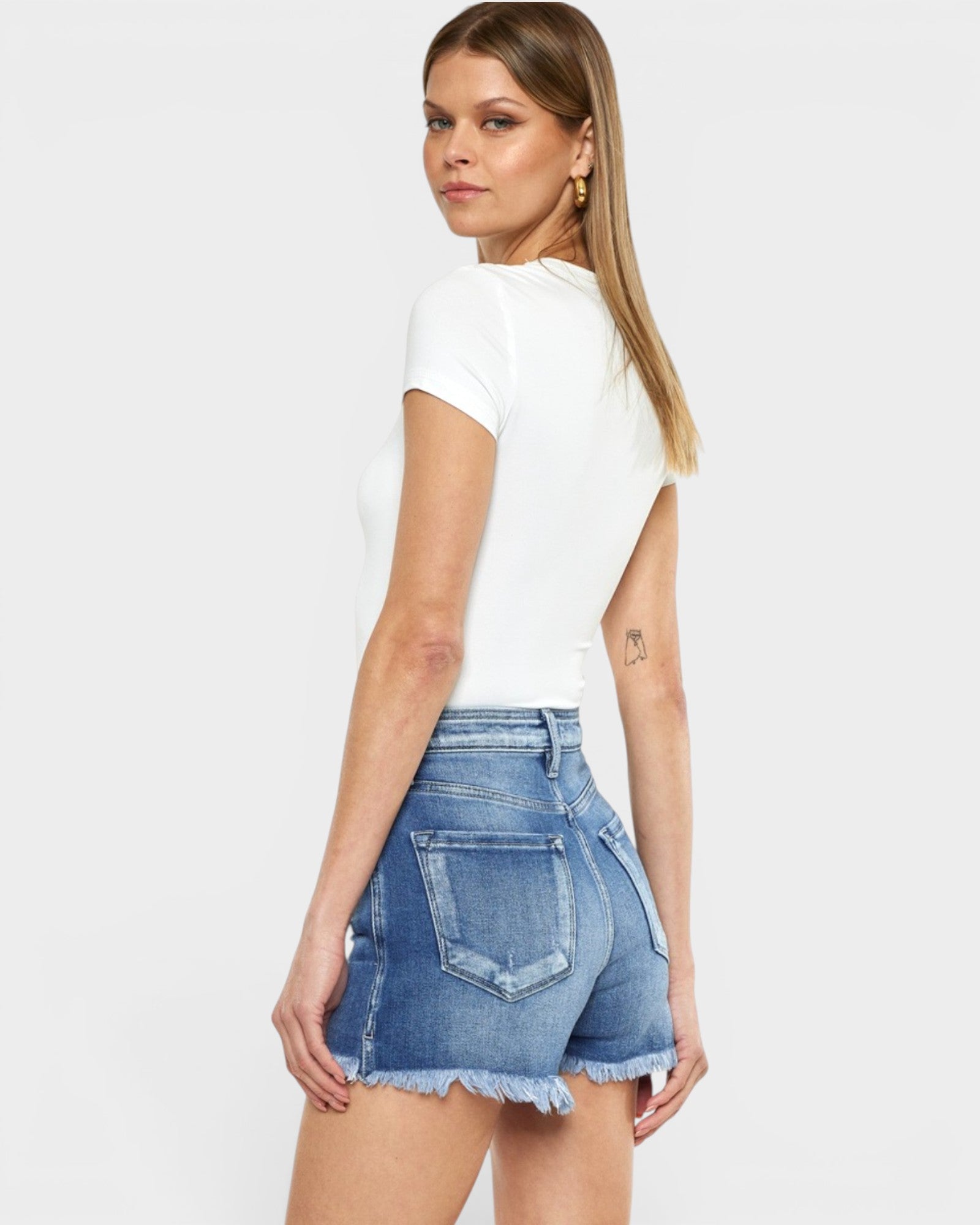 Woman wearing a white t-shirt and denim shorts on a plain background