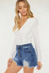 Woman wearing a white long-sleeve top and blue denim shorts on a white background