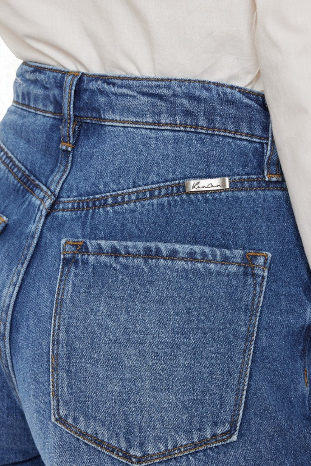Close-up of blue jeans with a brand label on the pocket, worn by a person.