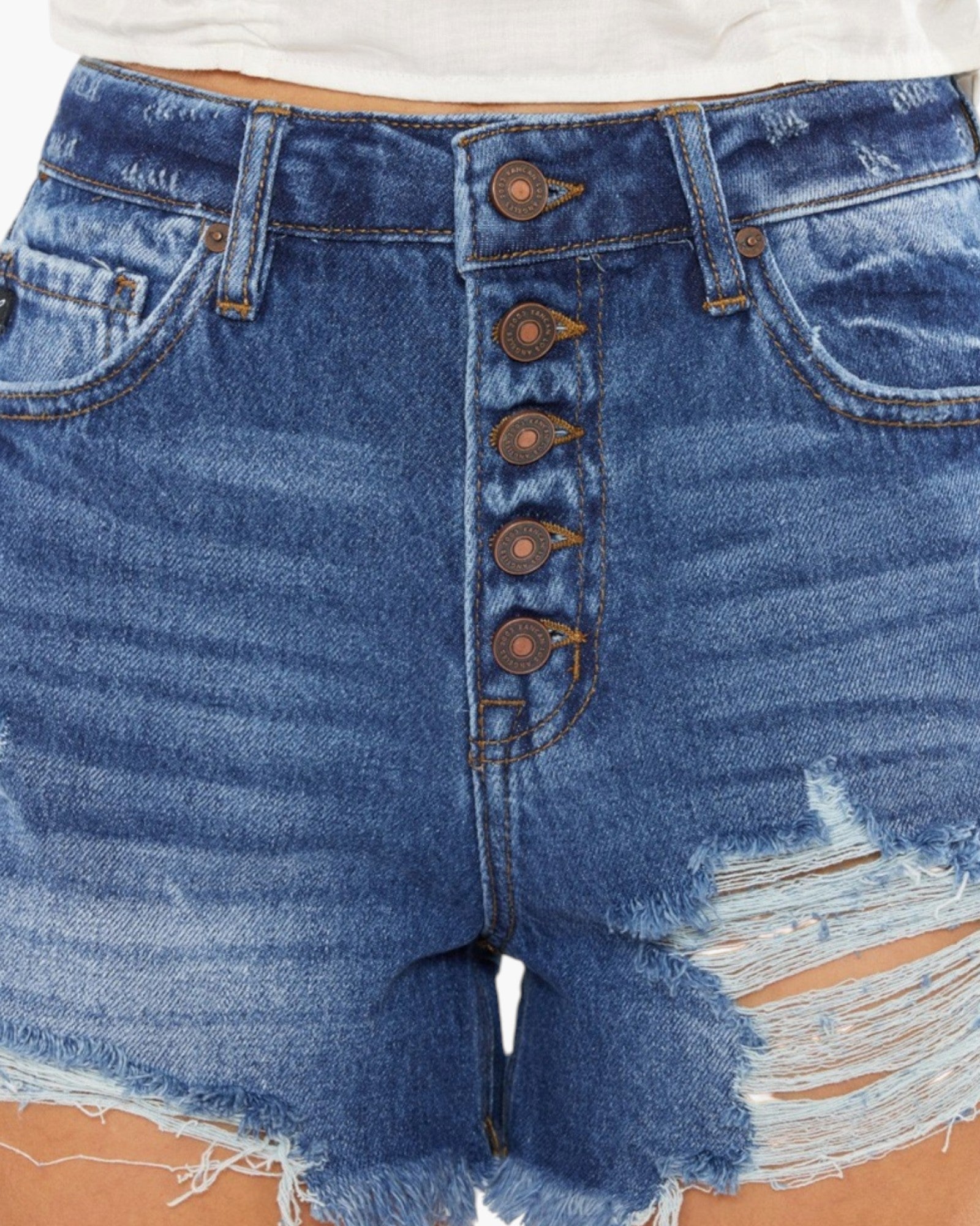 Close-up of blue denim shorts with a high-waisted fit, five front decorative buttons, distressed details, and frayed hems.
