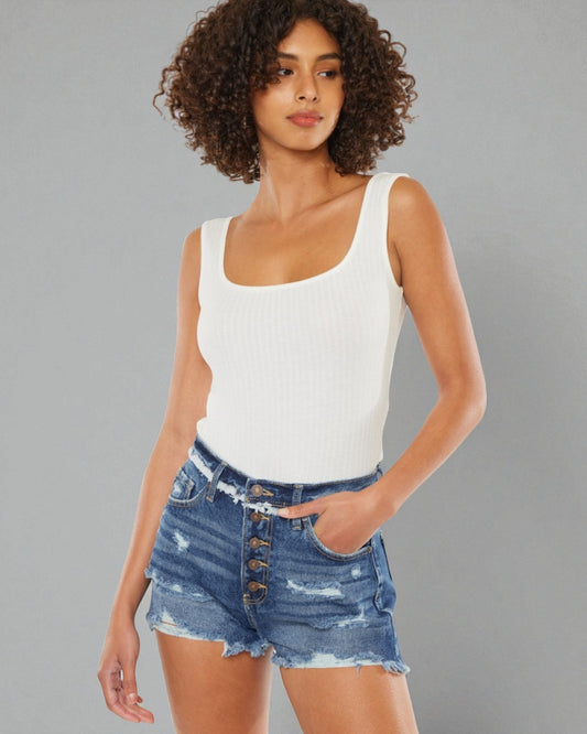 Woman wearing a white tank top and denim shorts against a gray background