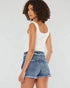 Woman wearing a white tank top and denim shorts on a plain background