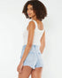 Woman wearing a white tank top and light blue denim shorts on a white background
