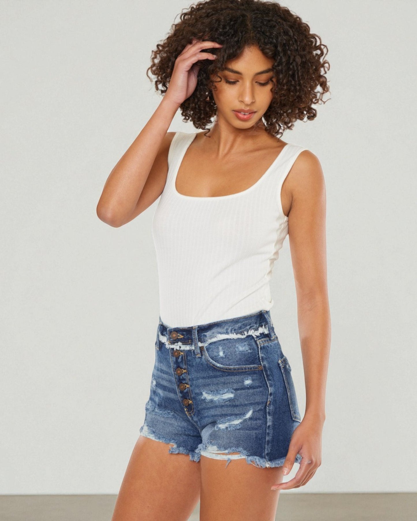 Woman wearing a white tank top and denim shorts against a plain background