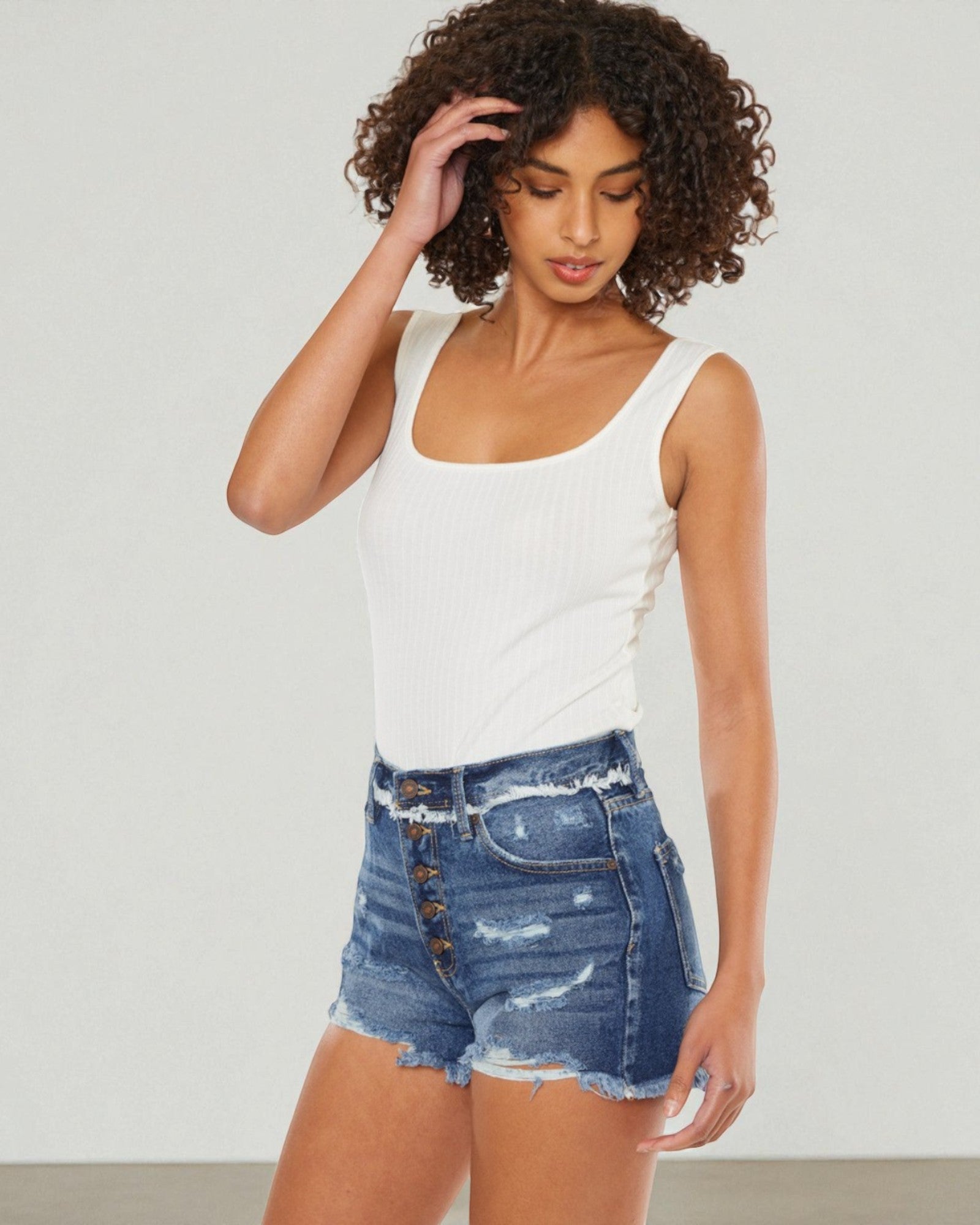 Woman wearing a white tank top and denim shorts against a plain background
